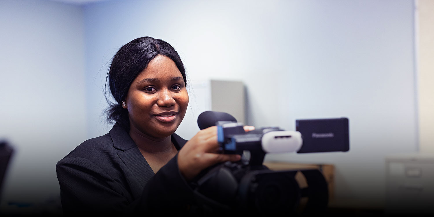 A smiling student in the classroom holding a camera